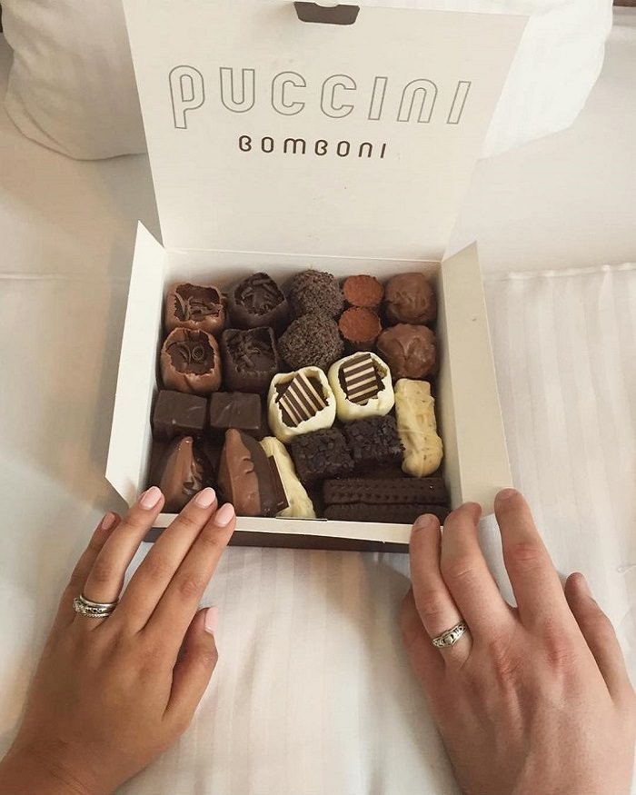 A married couple with a large box of Puccini Bomboni with 2 flavors of each bonbon